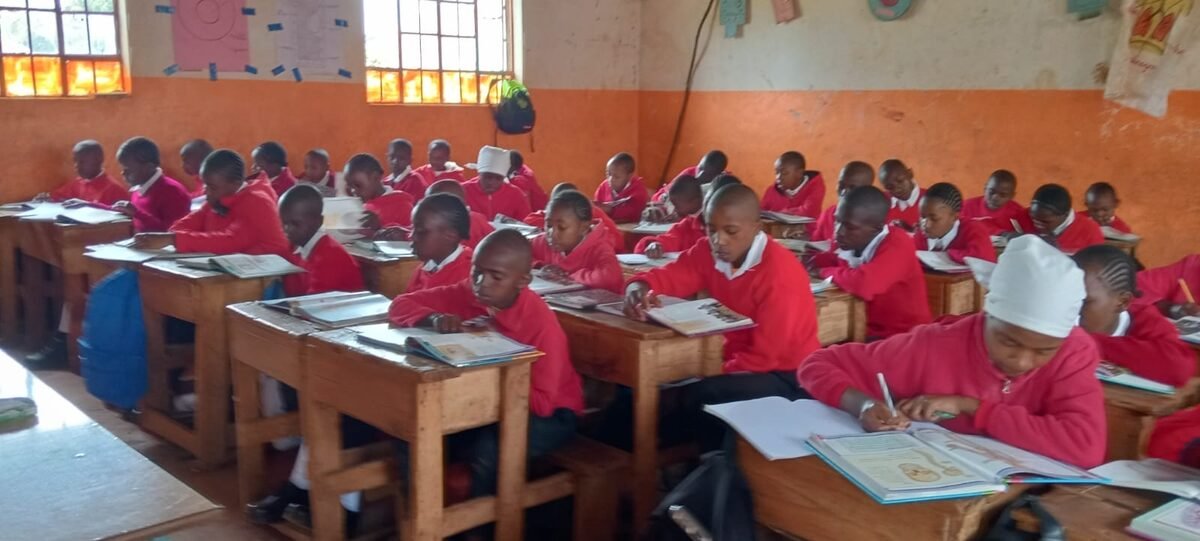Students in red uniforms studying with books in a Kenyan classroom supported by Global Abiding Hope