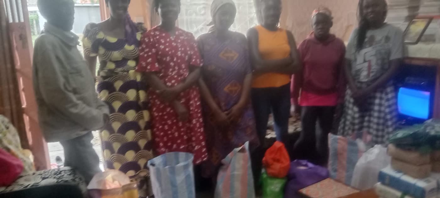 Women standing together indoors beside bags of food and household supplies