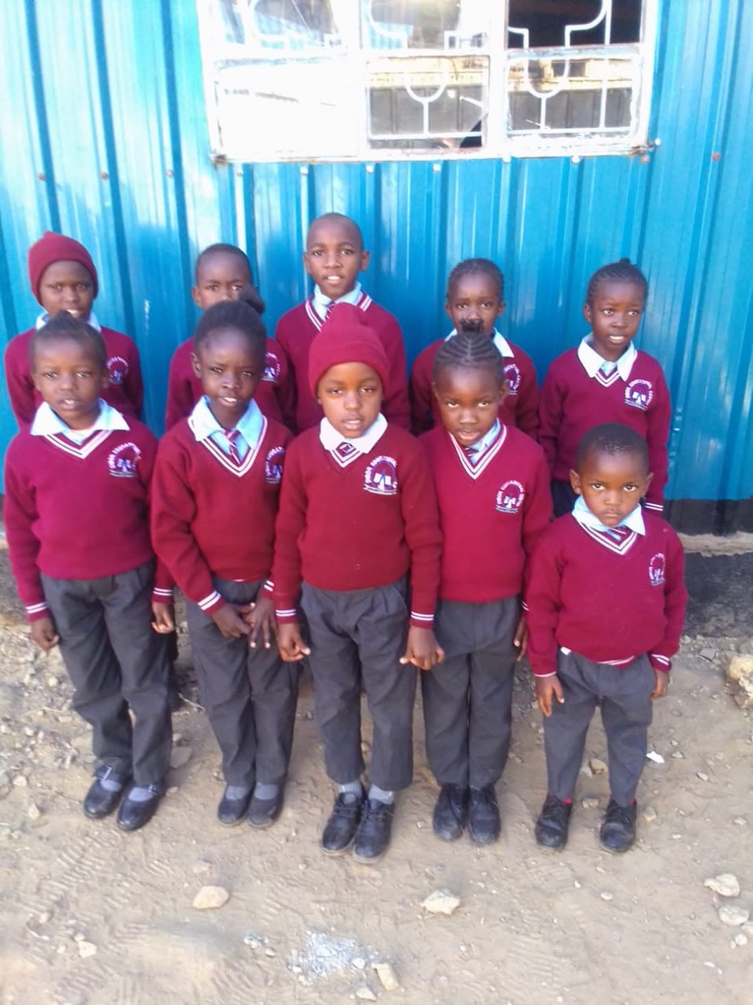Primary pupils in maroon uniforms standing together outside their classroom