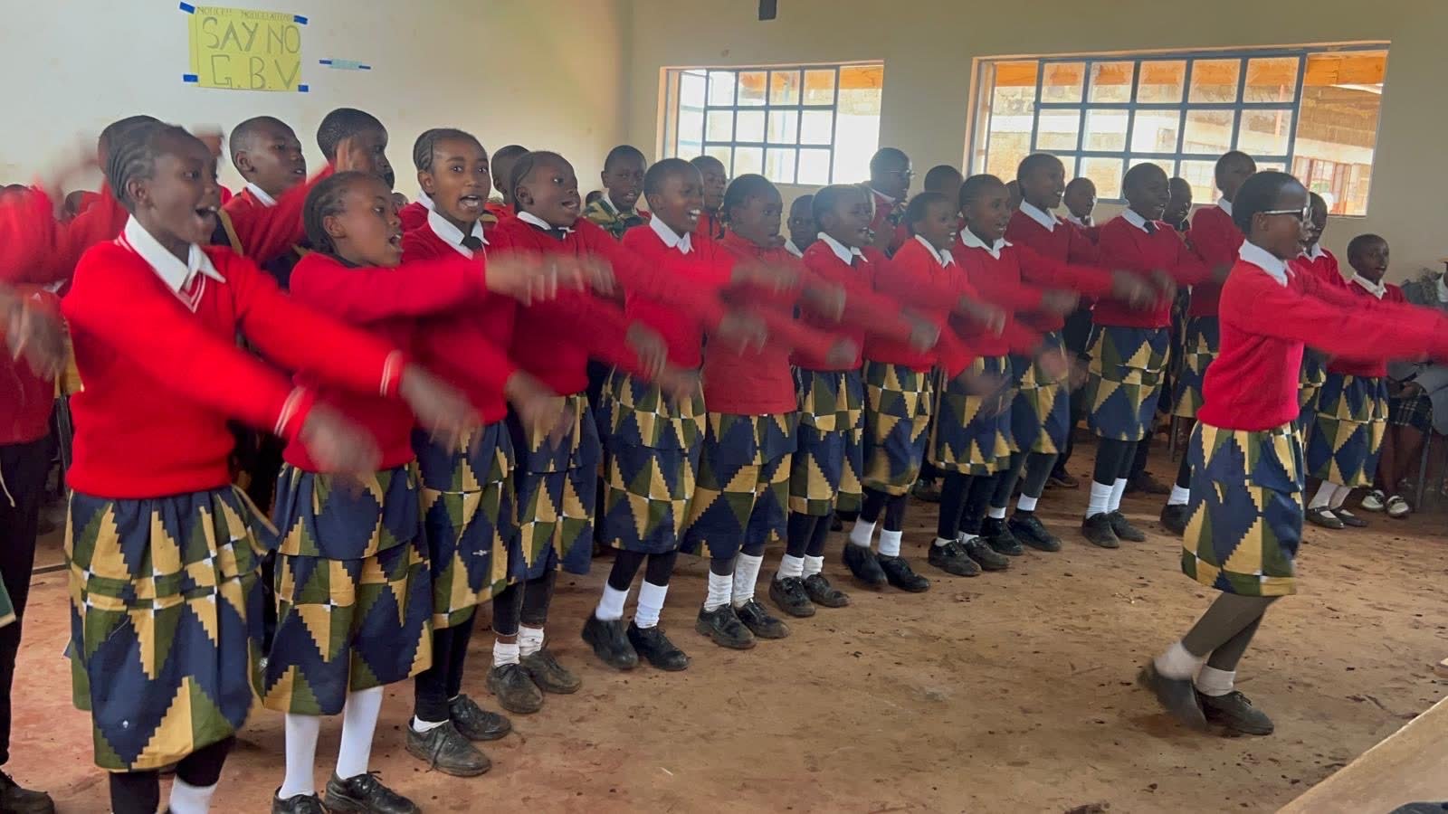 Students performing a dance in patterned uniforms inside the school hall