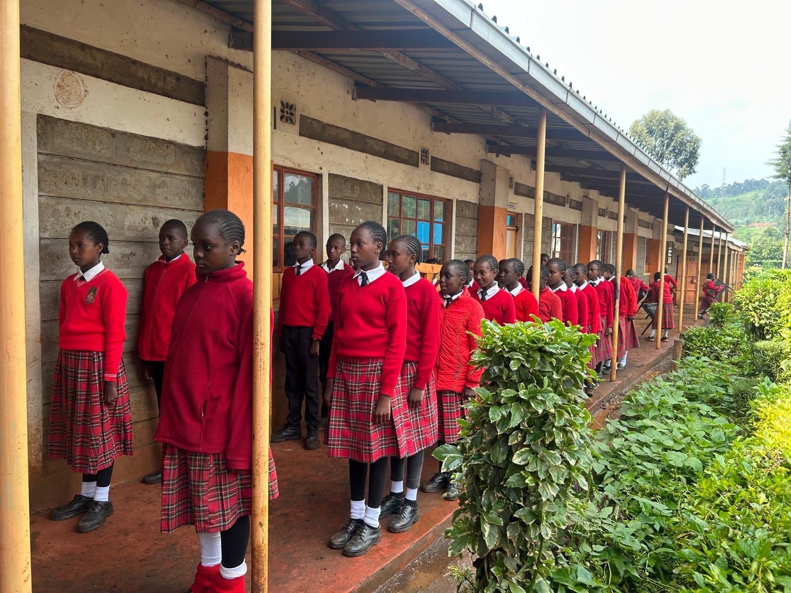 Students in red uniforms lined up along a school verandah in the morning