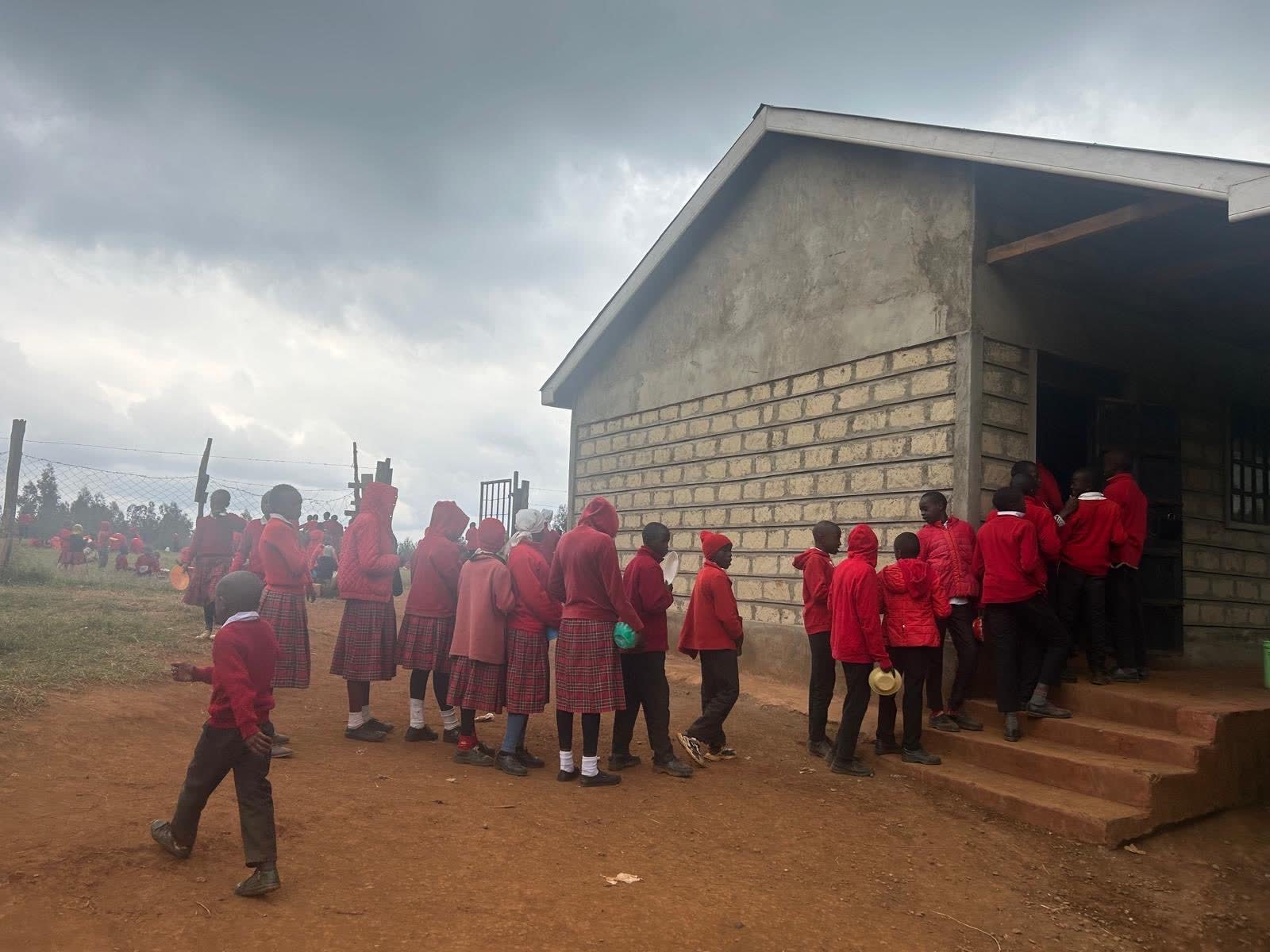 Students in red uniforms lining up with bowls outside the new school kitchen in Kenya