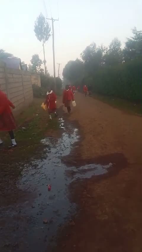 Schoolchildren in red uniforms walking to collect water, carrying containers